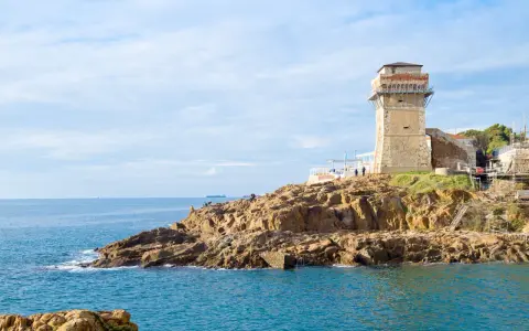Torre medievale e mare blu a Calafuria, con scogli rocciosi e cielo nuvoloso.