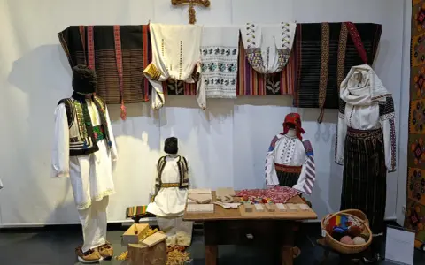 A Bucarest a dicembre, un'esposizione di abiti tradizionali rumeni, con manichini che indossano ricchi ricami e tessuti colorati.