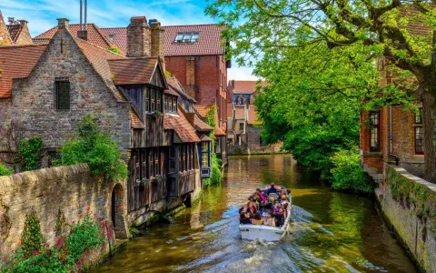 Giro in barca sui canali di Bruges, un'ottima idea per cosa vedere a Bruges in un giorno, tra case storiche e vegetazione lussureggiante.
