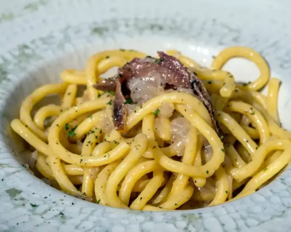 Bucatini con acciughe e cipolla, un classico tra i piatti tipici di Padova, conditi con prezzemolo fresco.