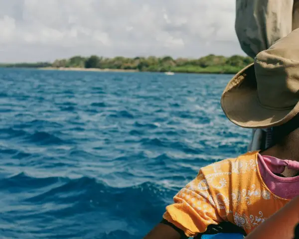 Persona con cappello di paglia osserva il mare blu e la costa verde. Un viaggio in Kenya è un'ottima idea per godersi questo panorama.