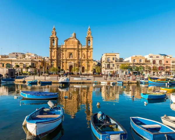 Barche colorate nel porto di Marsaxlokk, Malta. Un luogo incantevole dove dormire a Malta, con la chiesa barocca che domina lo sfondo.