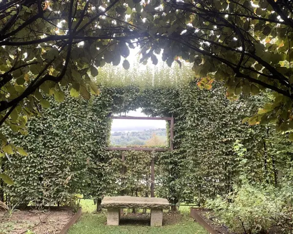 Un angolo verde incantevole, con un sedile in pietra che invita alla contemplazione del paesaggio visibile attraverso un'apertura nella siepe, come una finestra sul **palazzo di Cuzzano**.