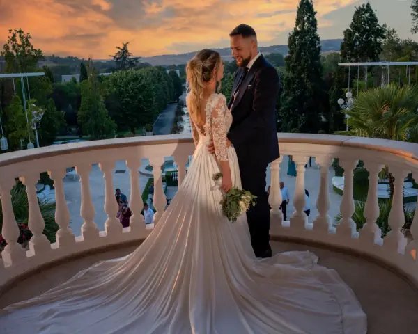 Coppia felice sul balcone al tramonto, con un abito da sposa da favola. Il loro fidanzamento ufficiale è celebrato in un'atmosfera magica.