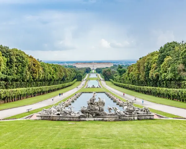 Giardini maestosi con fontane barocche e un palazzo imponente in lontananza, ricordano i fasti dei mulini reali.