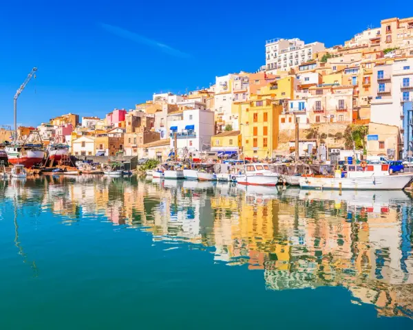 Porto di Sciacca, cosa vedere: barche da pesca ormeggiate e case colorate che si specchiano sull'acqua cristallina.