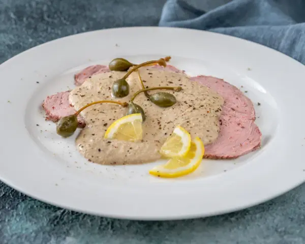 Vitello tonnato, uno dei piatti tipici torinesi, con salsa cremosa, capperi e limone su un piatto bianco.