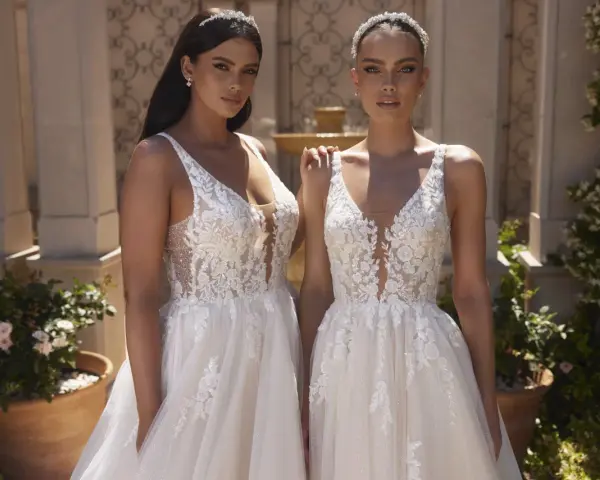 Due modelle con abiti da sposa in pizzo, con diversi tipi di scollatura a V e dettagli floreali, posano all'aperto.