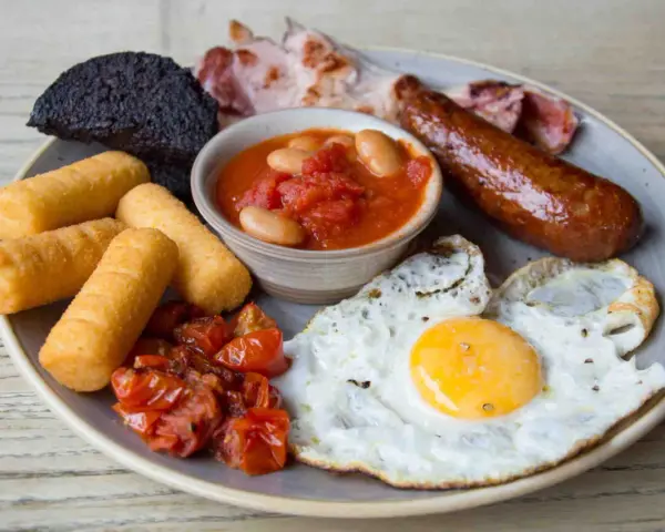 Un abbondante piatto per scoprire cosa mangiare a Londra: uova, salsiccia, fagioli, pomodorini, pane nero e crocchette.
