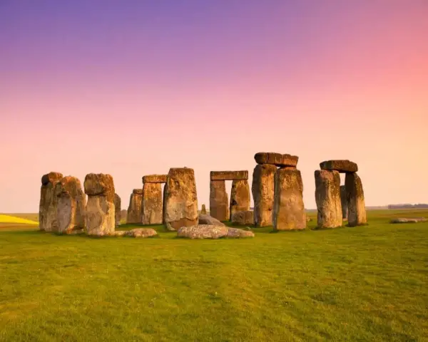 Stonehenge, un misterioso cerchio di pietre antiche, si erge su un prato verde sotto un cielo rosa e viola. Un'icona di Londra e della storia.