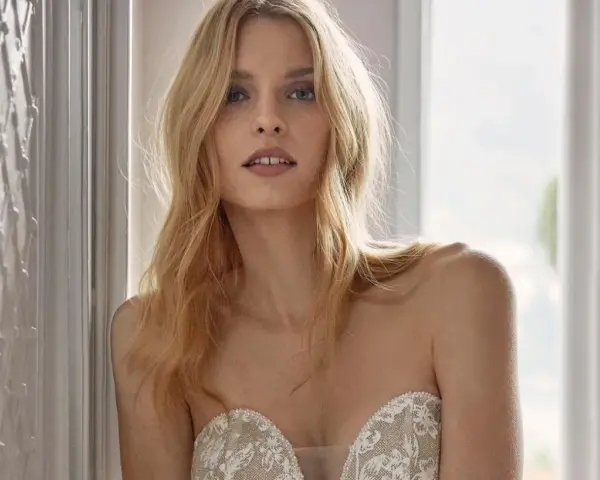 Modella con un trucco da sposa semplice, capelli biondi sciolti e un abito in pizzo.