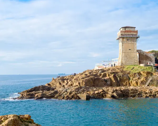 Torre medievale e mare blu a Calafuria, con scogli rocciosi e cielo nuvoloso.