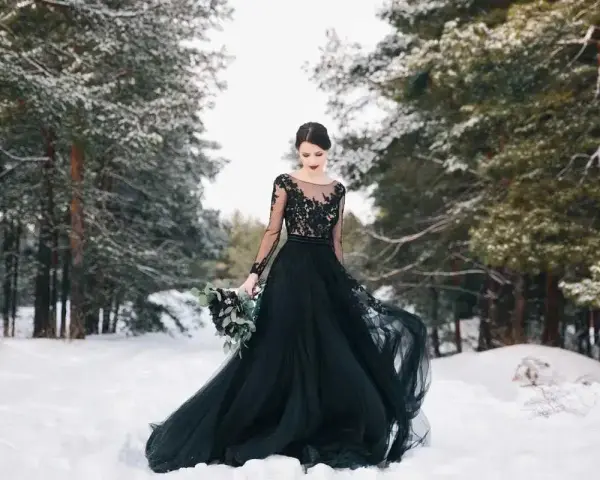 Una sposa in un bosco innevato indossa un abito da sposa nero, un simbolo di audacia e individualità.
