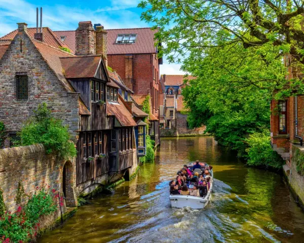 Giro in barca sui canali di Bruges, un'ottima idea per cosa vedere a Bruges in un giorno, tra case storiche e vegetazione lussureggiante.
