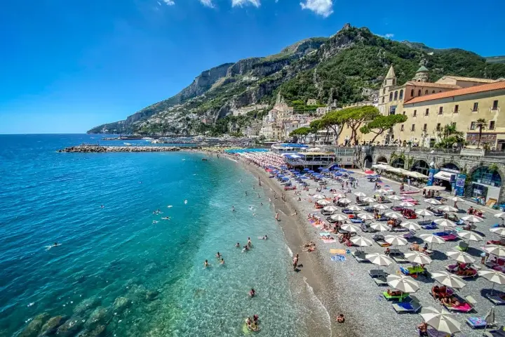 Spiaggia affollata con ombrelloni e gente che nuota, un'ottima idea per un weekend in Italia con vista sulla costa.