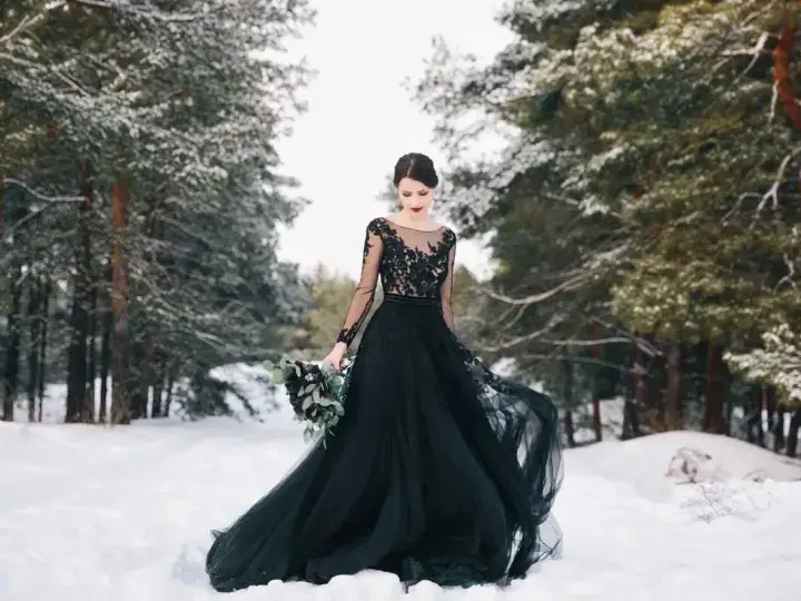 Una sposa in un bosco innevato indossa un abito da sposa nero, un simbolo di audacia e individualità.