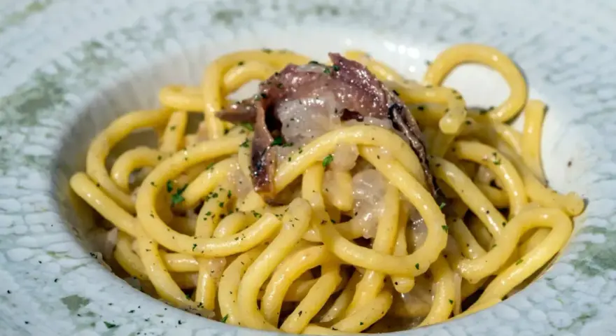 Bucatini con acciughe e cipolla, un classico tra i piatti tipici di Padova, conditi con prezzemolo fresco.