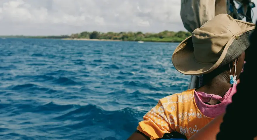 Persona con cappello di paglia osserva il mare blu e la costa verde. Un viaggio in Kenya è un'ottima idea per godersi questo panorama.