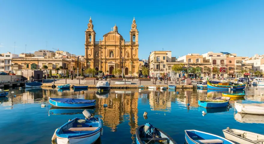 Barche colorate nel porto di Marsaxlokk, Malta. Un luogo incantevole dove dormire a Malta, con la chiesa barocca che domina lo sfondo.