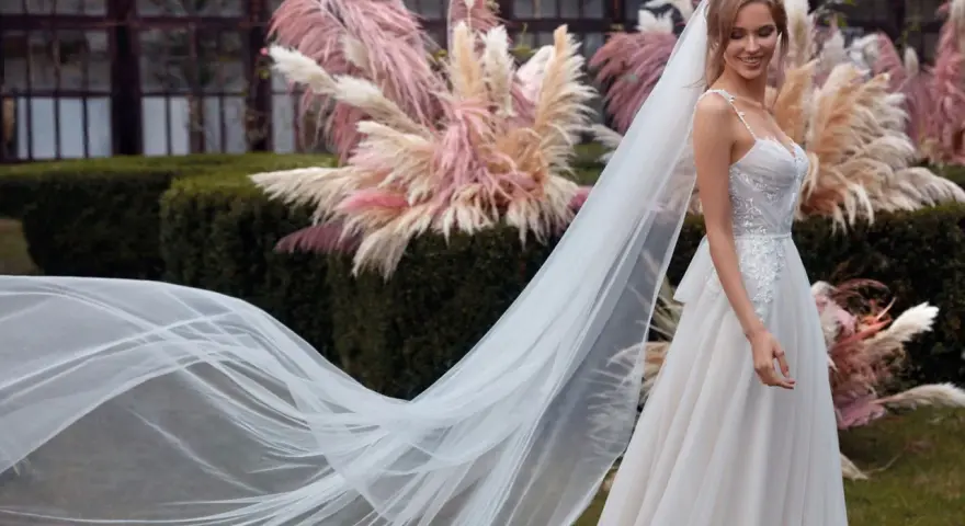 La sposa sorride, il suo abito bianco e il velo fluttuano dolcemente tra le pampas rosa.