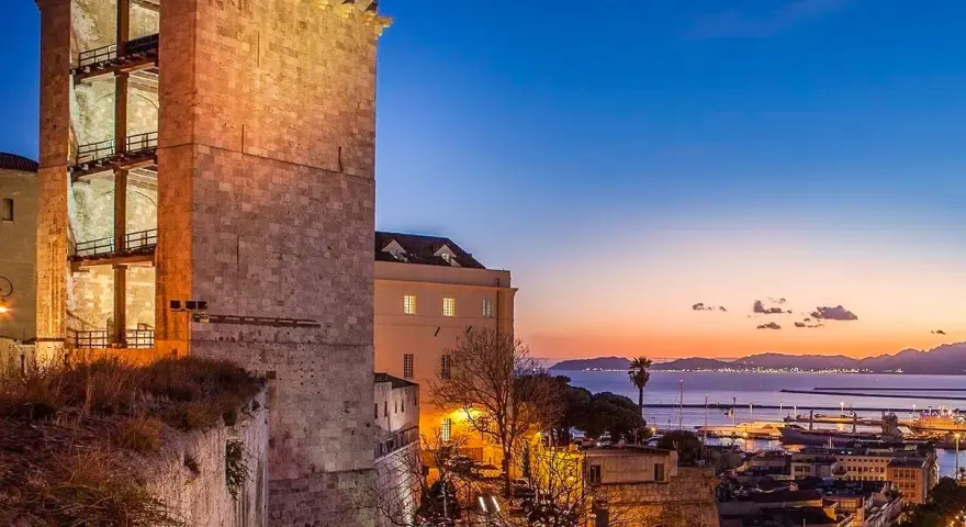 Torre medievale illuminata al tramonto, con vista sul porto e sul mare. Un'ottima anteprima di cosa vedere a Cagliari in un giorno.