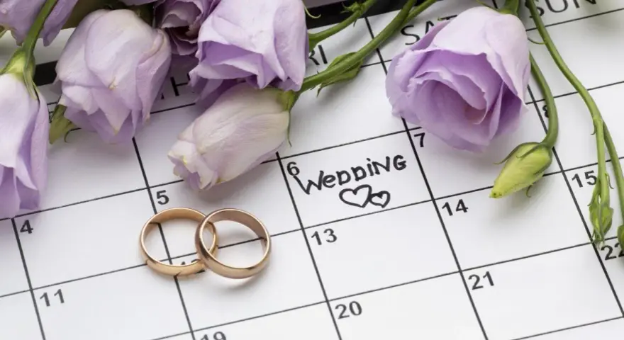 Anelli d'oro su un calendario segnato con "Wedding" e fiori lilla. Il giorno perfetto quando sposarsi.