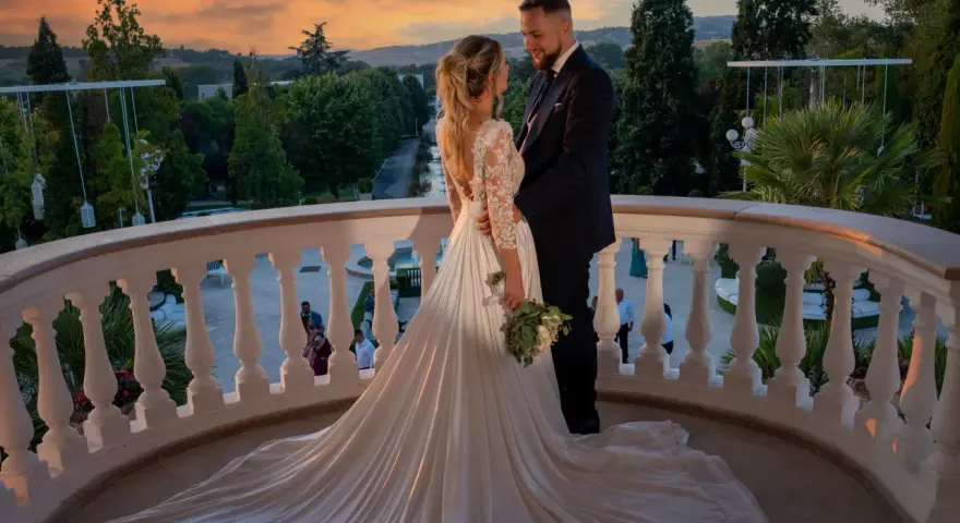 Coppia felice sul balcone al tramonto, con un abito da sposa da favola. Il loro fidanzamento ufficiale è celebrato in un'atmosfera magica.