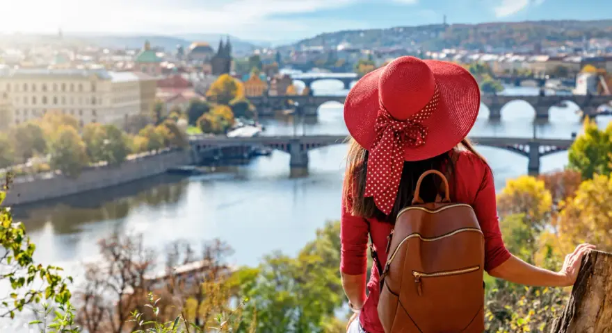 Donna con cappello rosso ammira Praga in autunno. Il periodo migliore per andare a Praga è quando la natura si tinge di colori caldi.