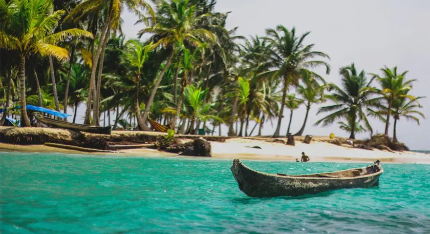 Barca in un mare turchese, palme e spiaggia. Un'idea perfetta per sapere dove andare al mare a Capodanno.