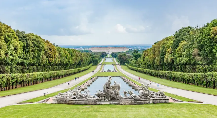 Giardini maestosi con fontane barocche e un palazzo imponente in lontananza, ricordano i fasti dei mulini reali.