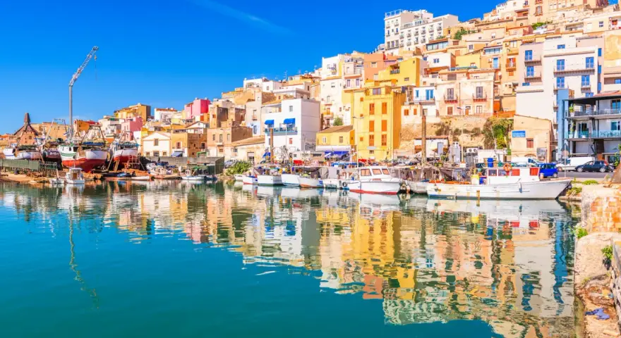 Porto di Sciacca, cosa vedere: barche da pesca ormeggiate e case colorate che si specchiano sull'acqua cristallina.