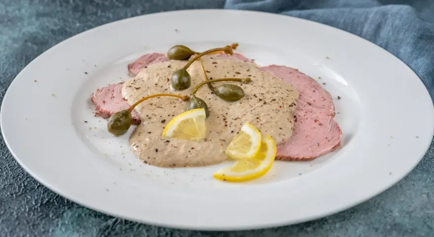 Vitello tonnato, uno dei piatti tipici torinesi, con salsa cremosa, capperi e limone su un piatto bianco.