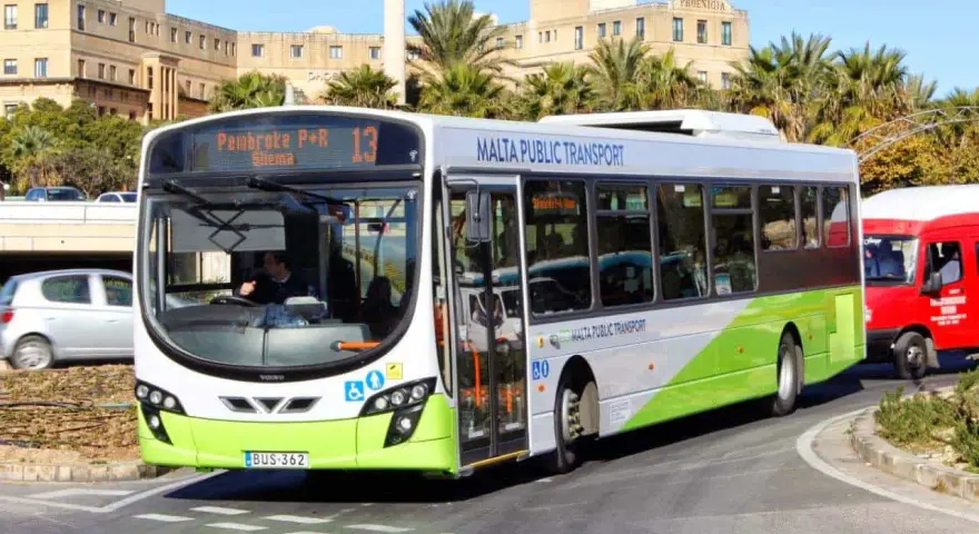Autobus bianco e verde di Malta Public Transport, ideale per scoprire come spostarsi a Malta. Percorre una strada con palme e edifici storici.