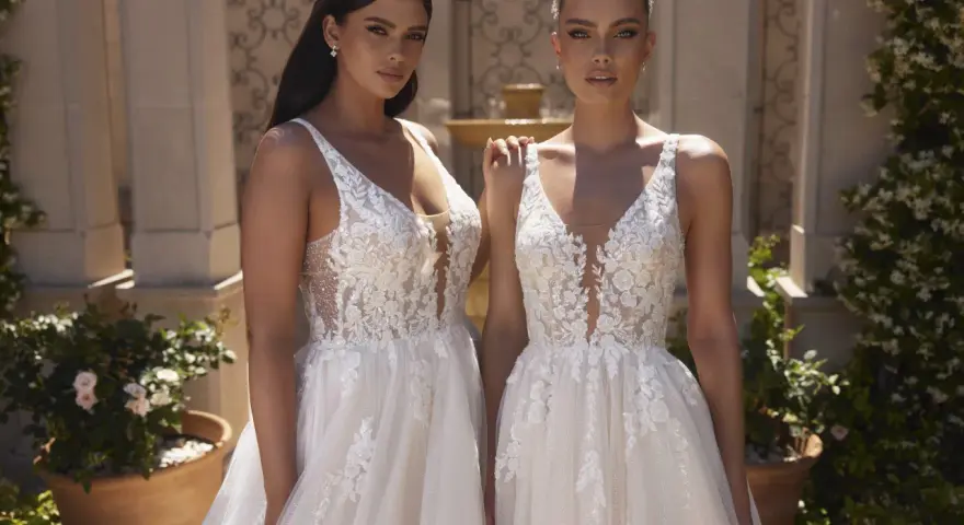Due modelle con abiti da sposa in pizzo, con diversi tipi di scollatura a V e dettagli floreali, posano all'aperto.