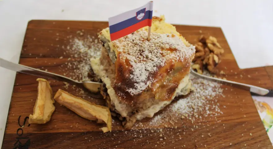 Una fetta di torta con bandierina slovena, noci e mele essiccate, un assaggio dei piatti tipici sloveni.