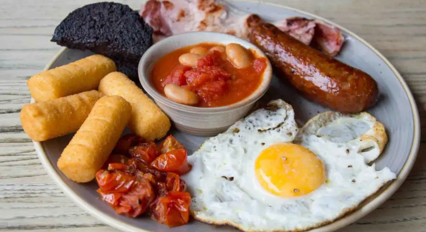 Un abbondante piatto per scoprire cosa mangiare a Londra: uova, salsiccia, fagioli, pomodorini, pane nero e crocchette.
