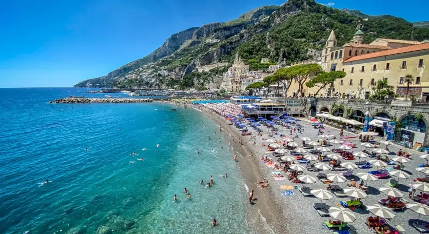 Spiaggia affollata con ombrelloni e gente che nuota, un'ottima idea per un weekend in Italia con vista sulla costa.