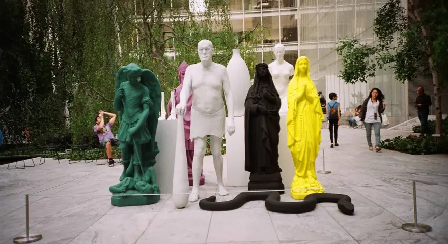 Sculture colorate e una figura in nero nel moma garden. Un serpente nero si snoda tra le statue.