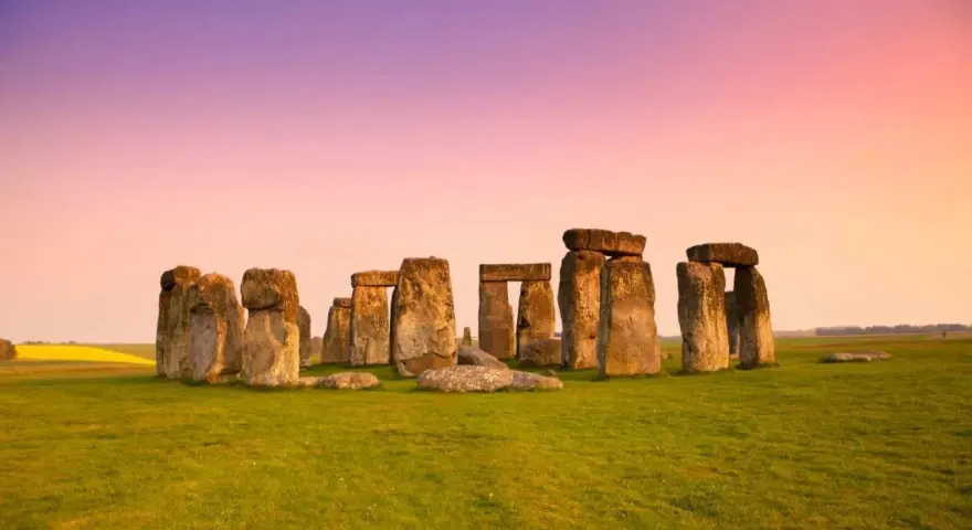 Stonehenge, un misterioso cerchio di pietre antiche, si erge su un prato verde sotto un cielo rosa e viola. Un'icona di Londra e della storia.