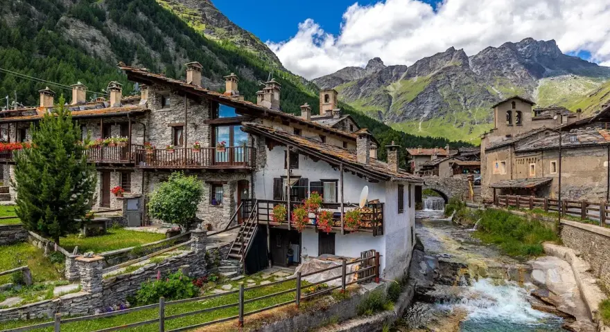 Un incantevole borgo da visitare in Piemonte, con case in pietra, balconi fioriti e un torrente che scorre tra le montagne.
