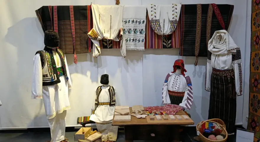 A Bucarest a dicembre, un'esposizione di abiti tradizionali rumeni, con manichini che indossano ricchi ricami e tessuti colorati.