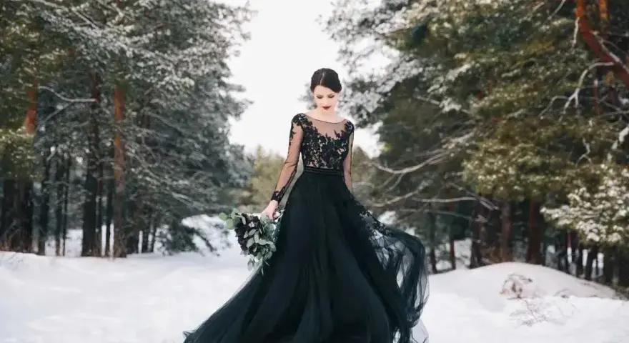 Una sposa in un bosco innevato indossa un abito da sposa nero, un simbolo di audacia e individualità.