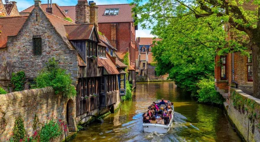 Giro in barca sui canali di Bruges, un'ottima idea per cosa vedere a Bruges in un giorno, tra case storiche e vegetazione lussureggiante.