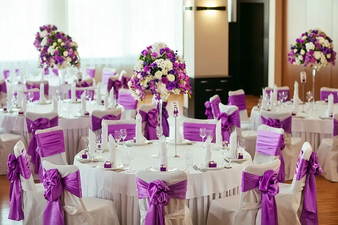 Allestimento elegante per nozze di viola, con tavoli rotondi, fiori lilla e sedie drappeggiate.