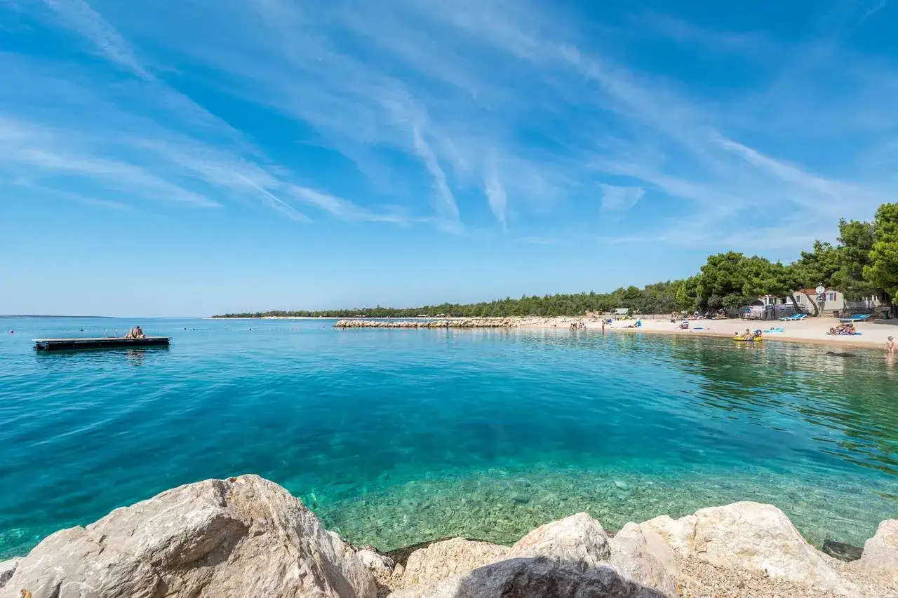 Spiaggia in Croazia dove andare: acque cristalline, sabbia dorata e pini marittimi. Perfetta per una vacanza rilassante.