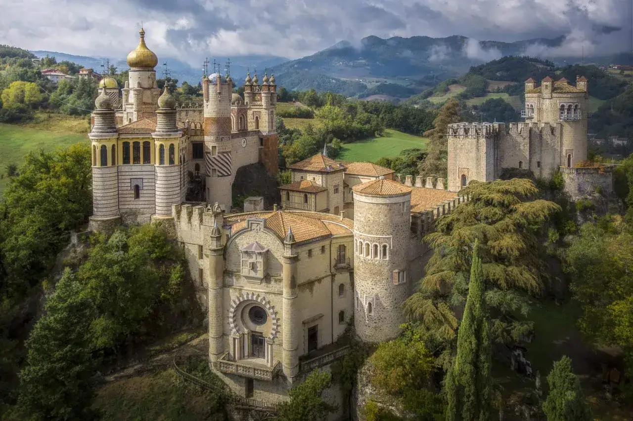 Il palazzo di Cuzzano, un castello fiabesco con torri dorate e mura antiche, domina un paesaggio collinare verdeggiante sotto un cielo nuvoloso.