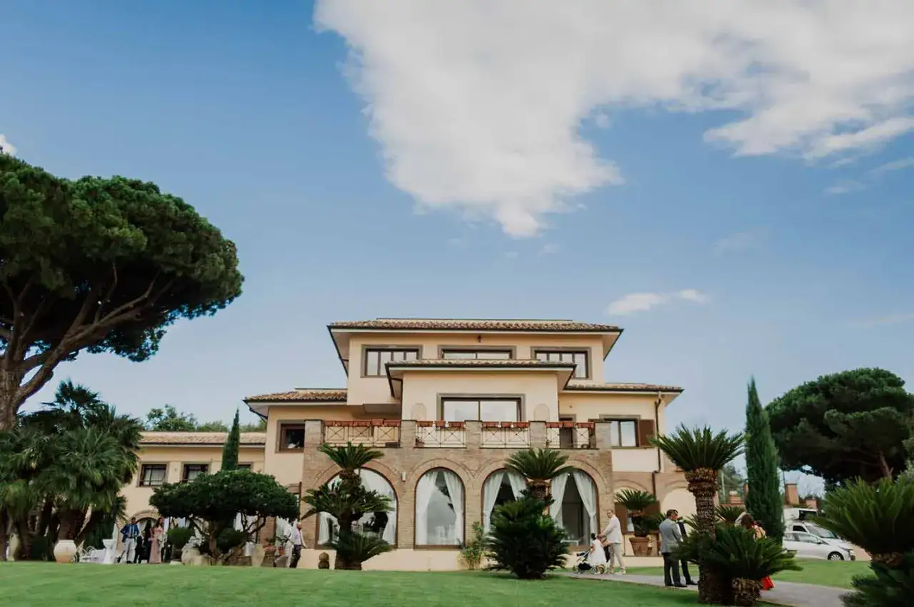 Un elegante edificio con archi e palme, parte del borgo della cartiera pontificia, accoglie ospiti sotto un cielo azzurro.