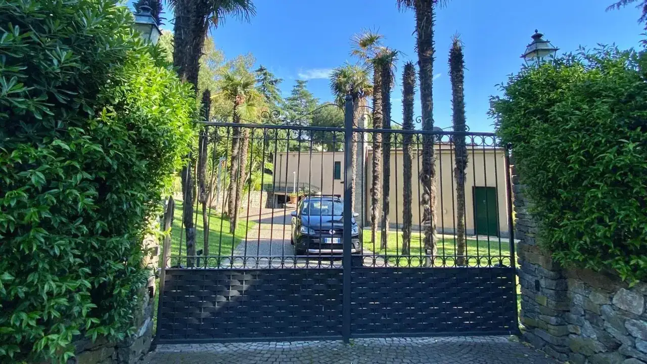 Cancello in ferro battuto di una villa Carrara a Genova, con palme e vegetazione lussureggiante.