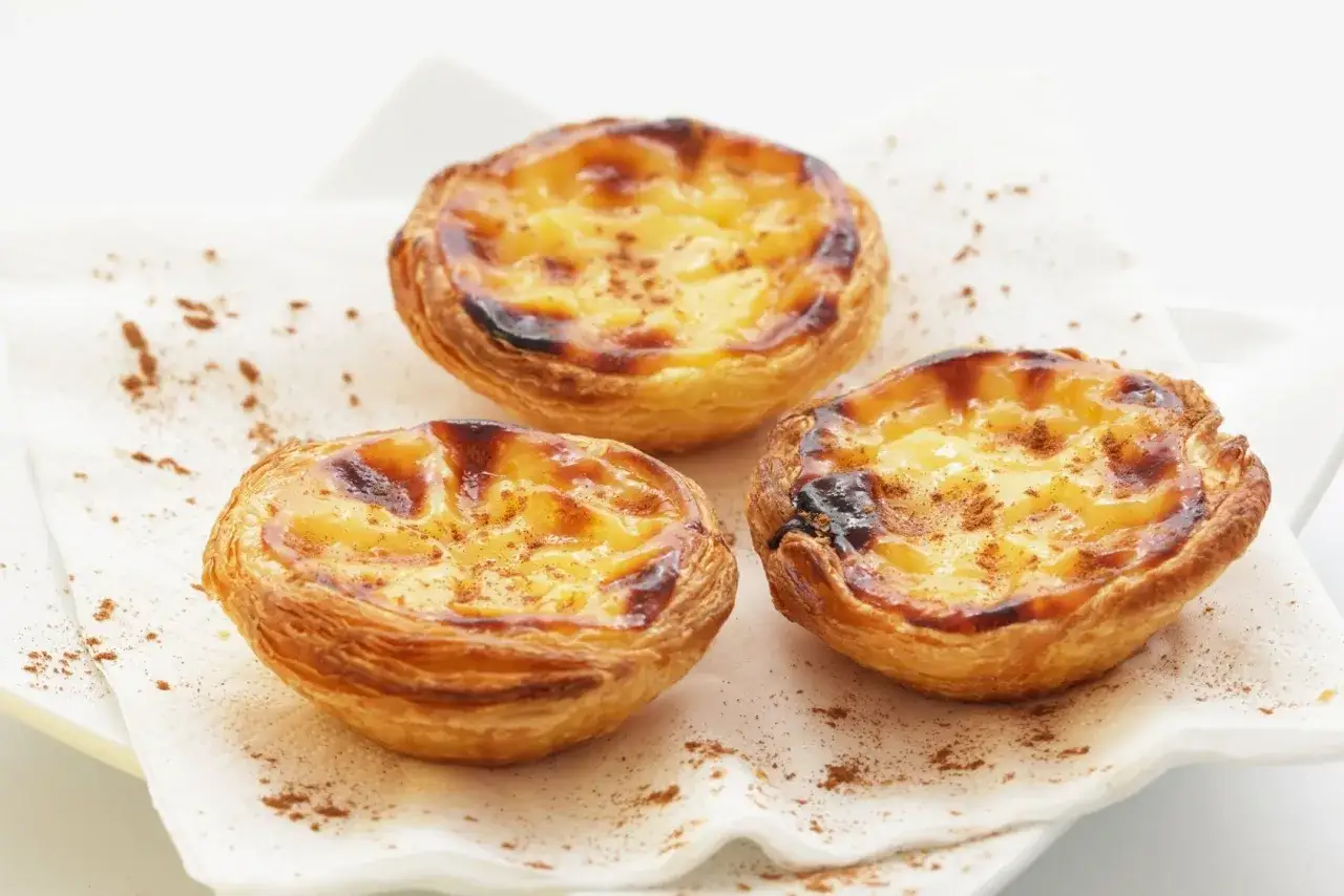 Tre deliziosi past&eacute;is de nata, un must per sapere cosa mangiare a Lisbona, cosparsi di cannella su un tovagliolo bianco.
