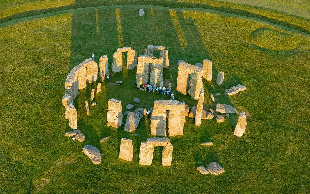 Stonehenge, vicino a Londra, illuminato dal sole del tramonto. Un cerchio di antiche pietre su un prato verde, con visitatori che ammirano il mistero.
